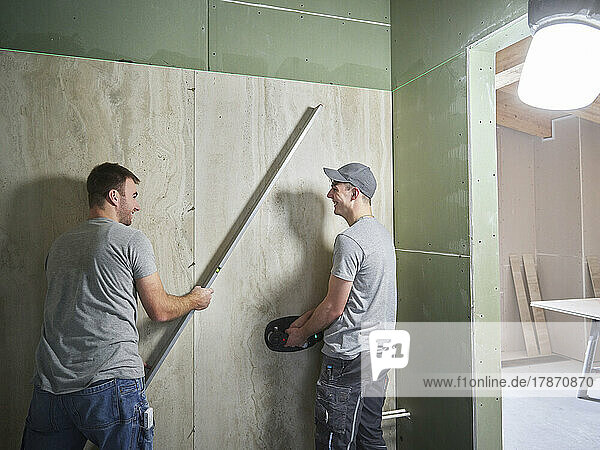 Happy tilers lifting large ceramic tiles onto wall with vacuum suction cups