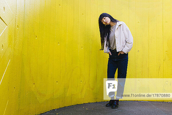 Young woman with head cocked standing in front of yellow wall
