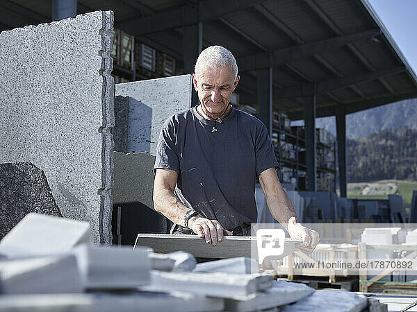 Smiling stonemason examining natural stone slab at workshop
