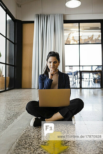 Young businesswoman sitting with hand on chin looking at laptop in office