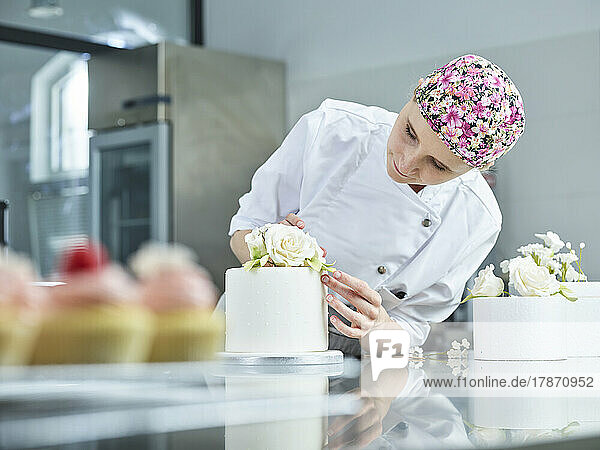 Confectioner decorating cake with marzipan roses in kitchen