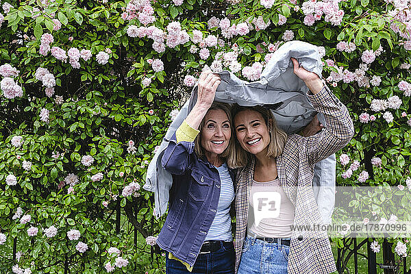 Smiling mother and daughter under windbreaker in front of flowers