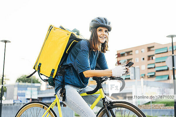 Smiling delivery person with mobile phone sitting on bicycle