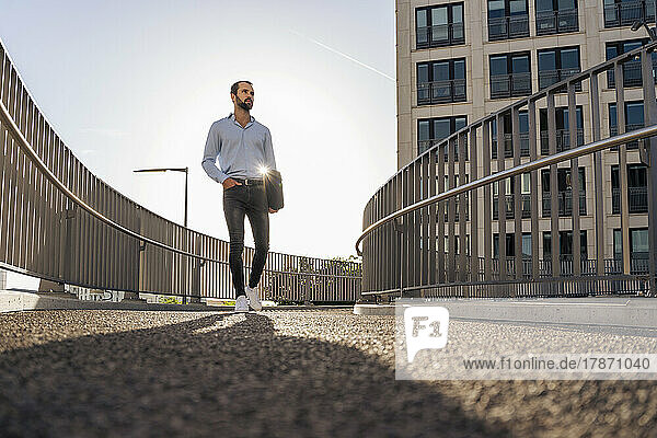 Young businessman with bag walking on footbridge