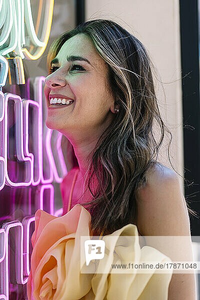 Cheerful young woman by illuminated neon lights