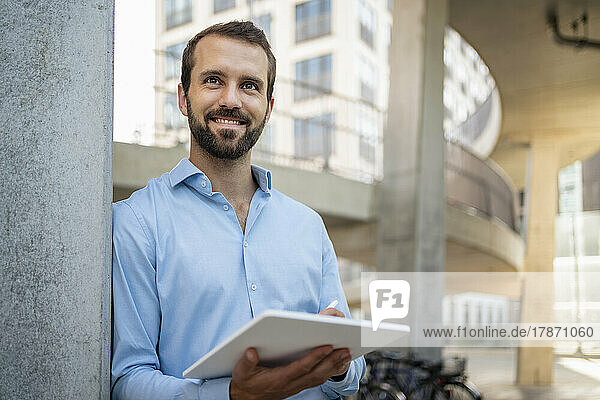 Glücklicher junger Geschäftsmann mit Tablet-PC  der unter einer Brücke steht