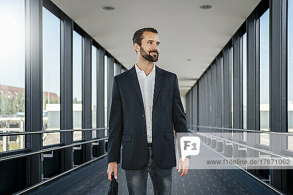 Smiling young businessman with bag walking on elevated walkway