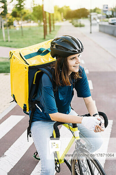 Lächelnde junge Lieferfrau  die auf dem Fahrrad sitzt