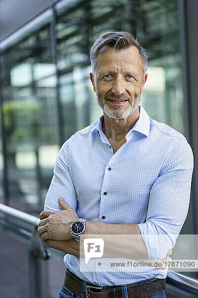 Confident businessman with arms crossed by railing