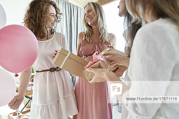 Lächelnde Freunde  die der schwangeren Frau ein Geschenk machen