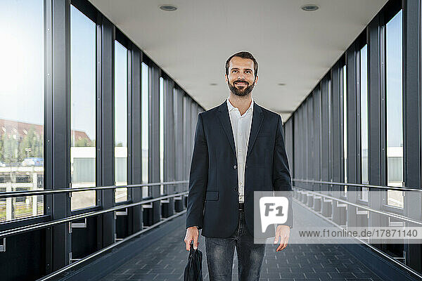 Smiling businessman with bag walking on elevated walkway