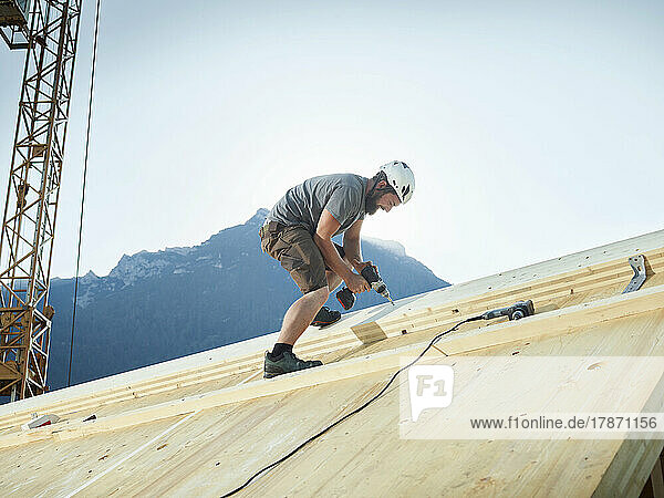 Carpenter working with drill on roof at construction site