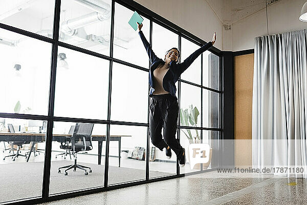 Happy young businesswoman jumping in office
