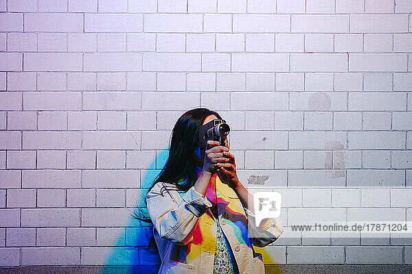Young woman filming with video camera in front of wall