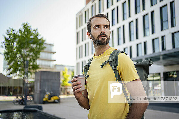Young man with disposable coffee cup standing outside building