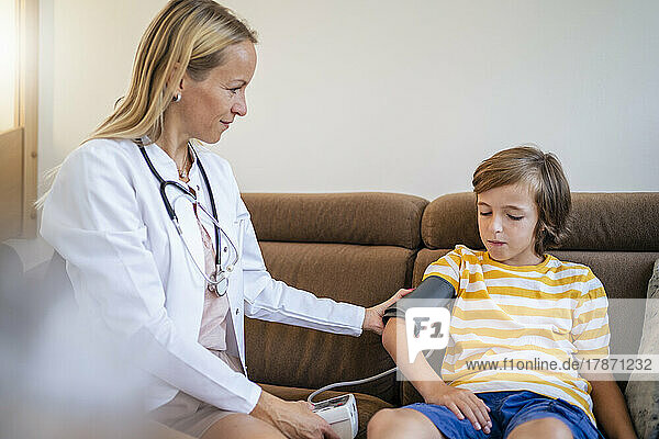 Female doctor taking boy's blood pressure on couch at home