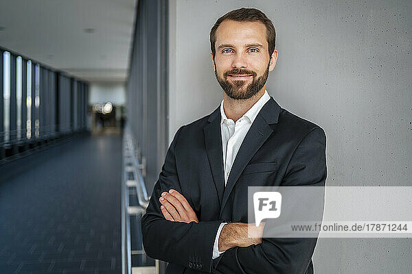 Smiling businessman with arms crossed standing in front of wall