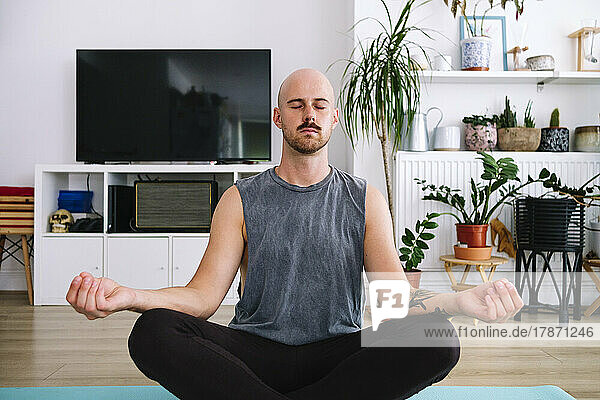 Bald man with eyes closed meditating in living room at home