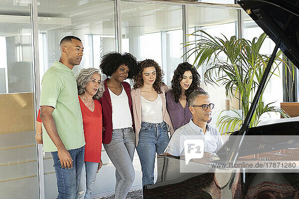 Businesswomen standing with businessman looking at colleague playing piano in office