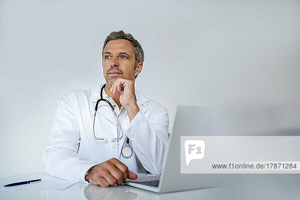 Pensive mature doctor sitting at desk in medical practice