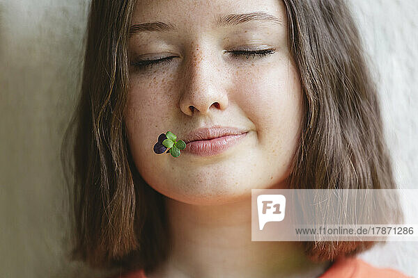Teenager-Mädchen mit geschlossenen Augen und Microgreens zwischen den Lippen