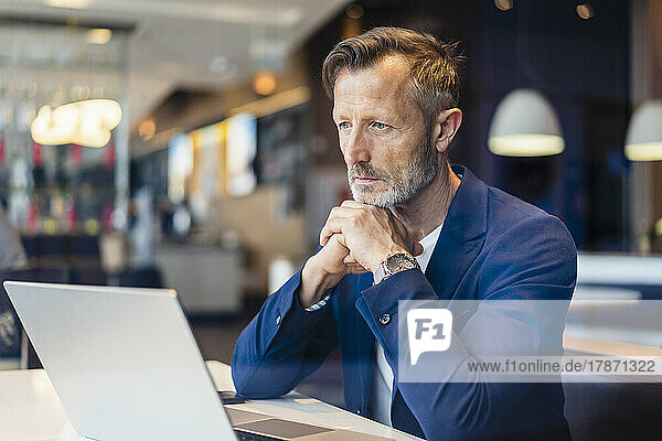 Contemplative businessman with laptop in cafe