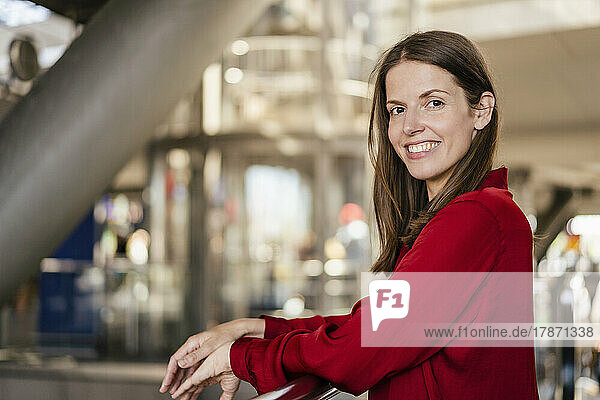 Smiling businesswoman leaning on railing in office