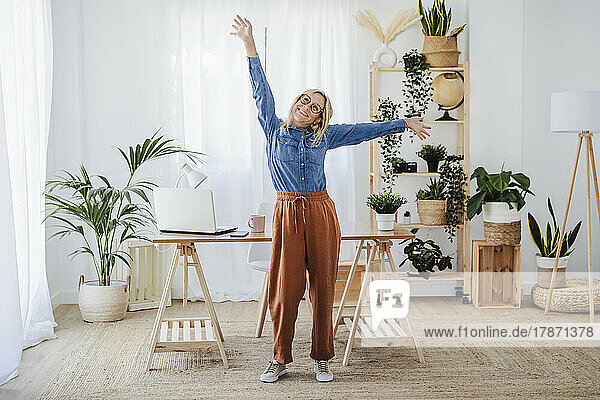 Happy freelancer with arms raised standing at home office