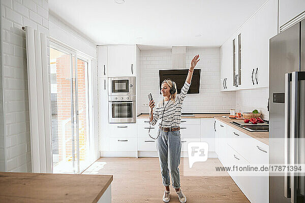 Woman listening music on headphones and dancing in kitchen