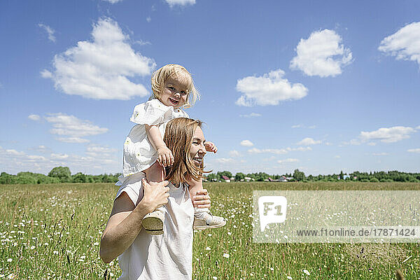 Smiling mother carrying daughter on shoulders at field