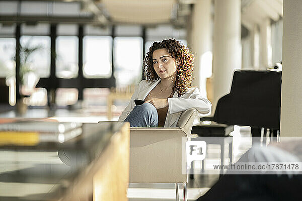 Thoughtful businesswoman with curly hair sitting on chair in office
