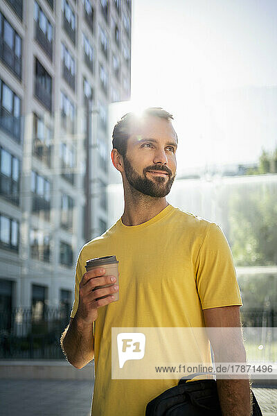 Smiling young businessman with coffee cup standing in front of building
