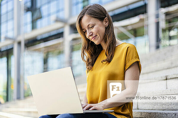 Smiling businesswoman using laptop sitting on steps