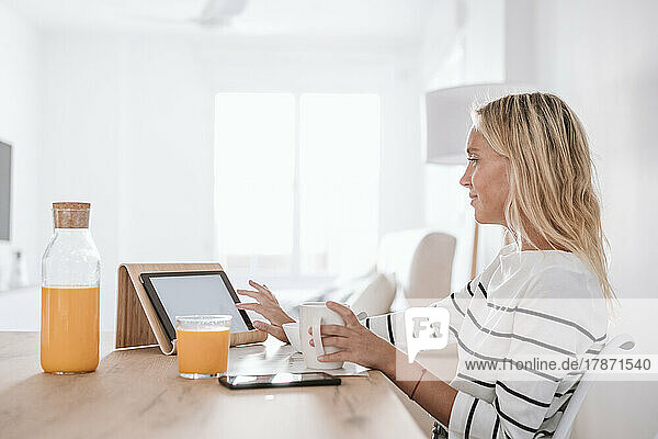 Young woman with coffee cup using tablet PC on table at home