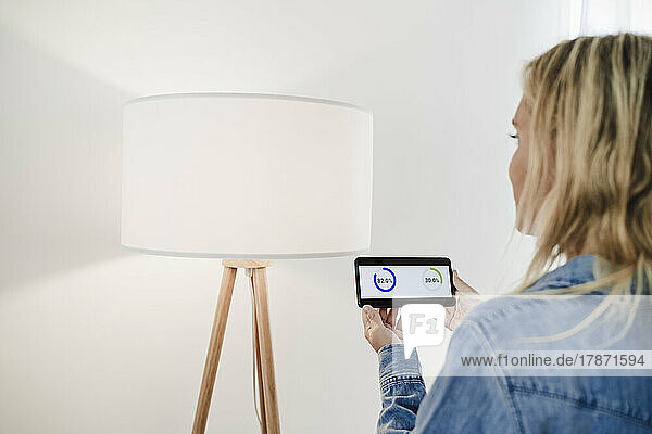 Woman checking electrical consumption of lamp on mobile phone app at home