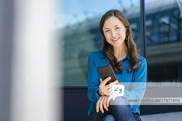 Frau mit braunen Haaren hält Smartphone in der Hand