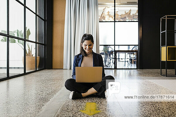 Smiling young businesswoman working on laptop at office