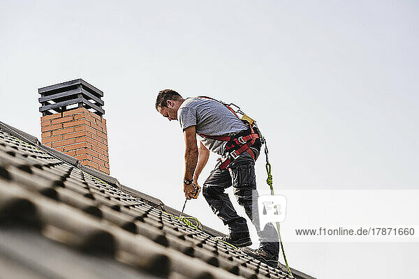 Electrician tying rope standing on roof