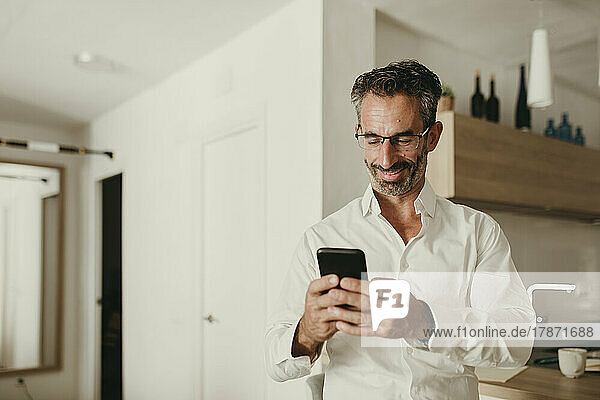 Smiling businessman using smart phone in kitchen at home