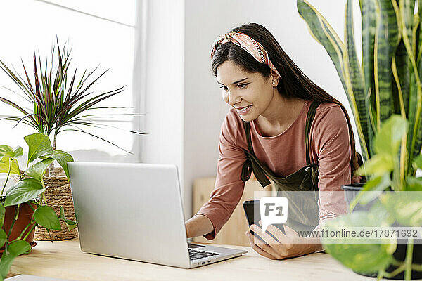 Smiling woman using laptop by potted plants on table at home