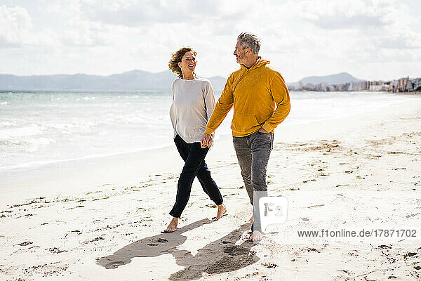 Smiling woman with man holding hands and walking on shore at beach