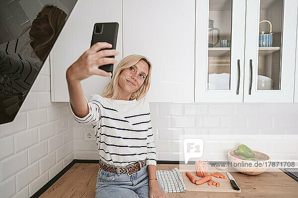 Smiling young woman taking selfie on smart phone at home