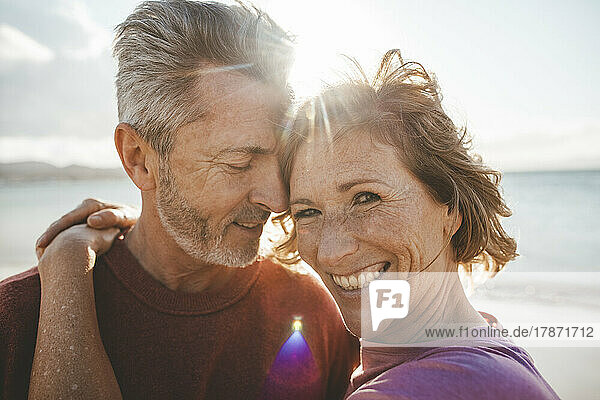 Glücklicher reifer Mann umarmt Frau am Strand an einem sonnigen Tag