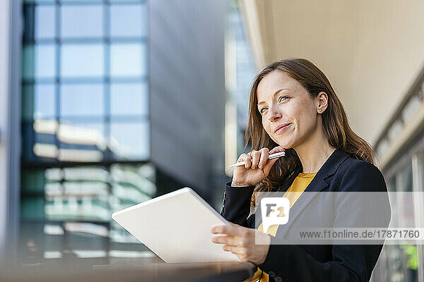 Smiling businesswoman with hand on chin holding tablet PC