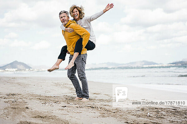 Mature man with woman enjoying piggyback ride at beach