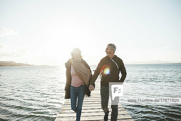 Happy mature couple holding hands walking on jetty