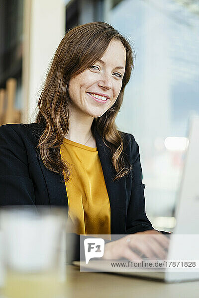Smiling businesswoman with laptop at cafe