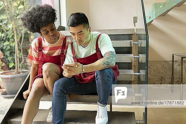Mann teilt Smartphone mit Kollege  der auf Stufen im Café sitzt