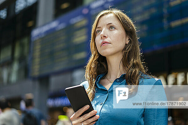 Contemplative woman holding smart phone on sunny day