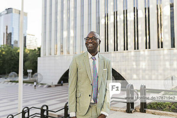 Happy mature businessman standing in front of building at financial district